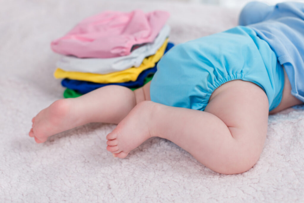 The child lies near a stack of multi-colored cloth diaper covers on a changing table