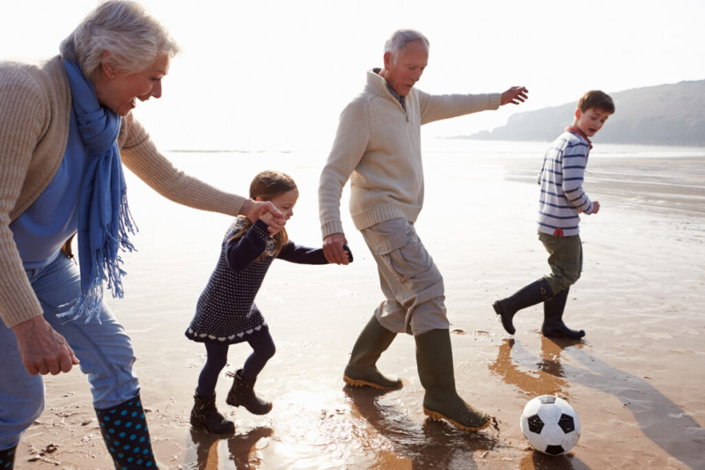 grandparents at beach with two grandkids, kicking soccer ball in the low tide