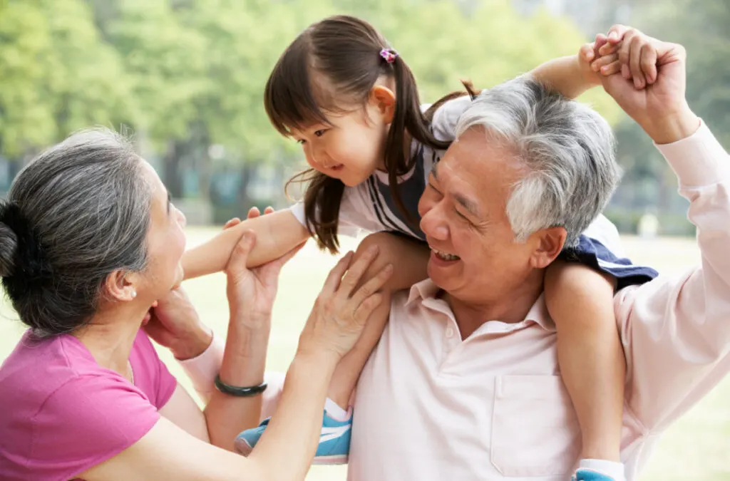 Asian grandparents happily spending time with grandchild, who is sitting on grandfather's shoulders