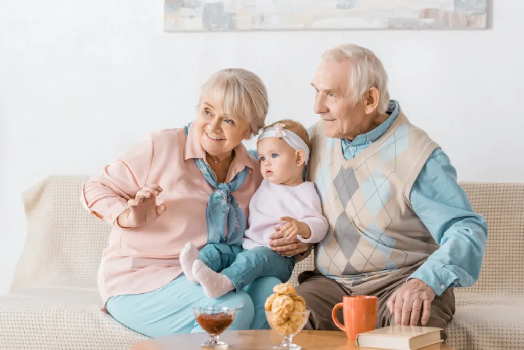 grandparents sitting on couch holding grandchild, smiling
