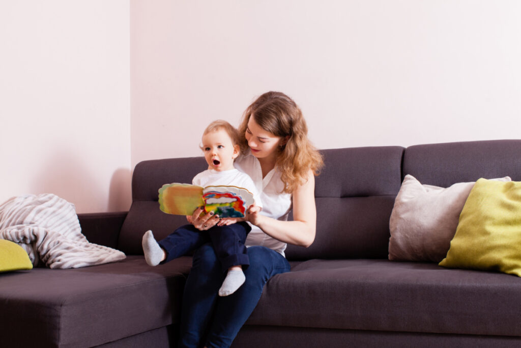 young mom sitting on couch reading Boynton board books to baby