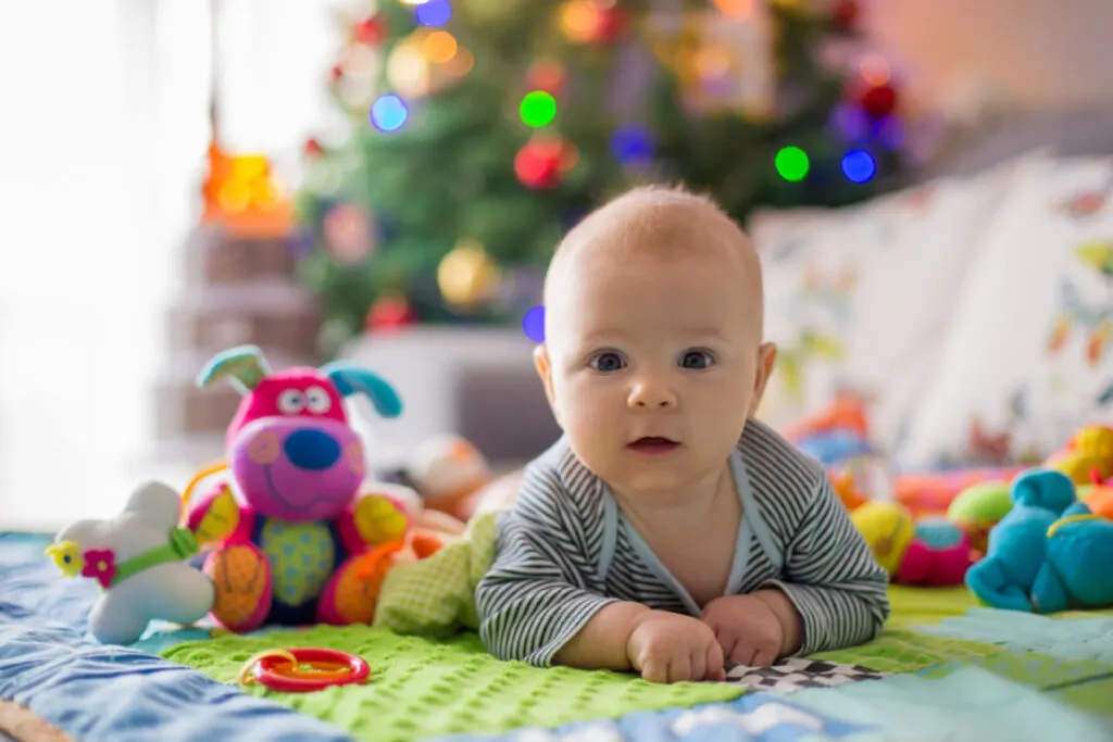 happy baby on play mat in front of Christmas tree surrounded by toys