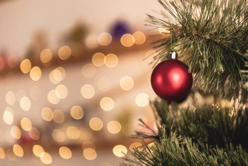 red ball Christmas ornament with warm Christmas lights in the background for baby's first Christmas