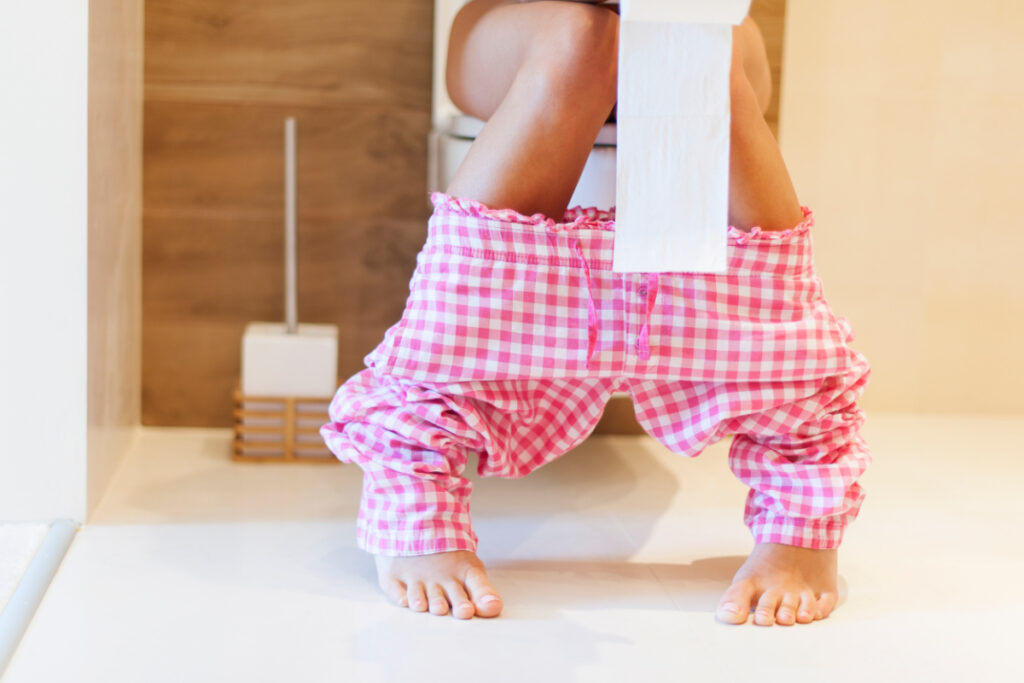 woman sitting on toilet wearing pink gingham pants, unable to urinate after birth