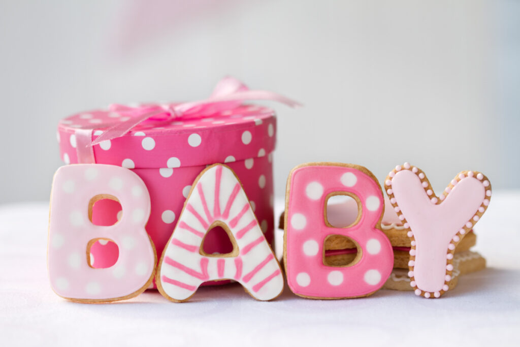 frosted cookies spelling "Baby" next to baby shower gift in pink polka dot wrapping paper
