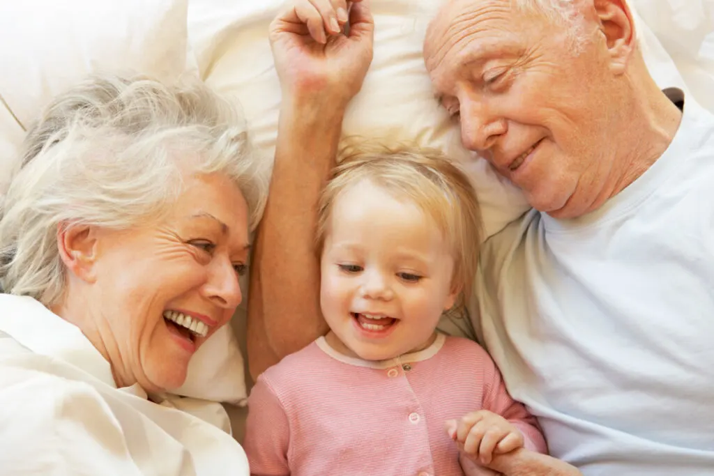 grandparents happily babysitting granddaughter, snuggling in bed together