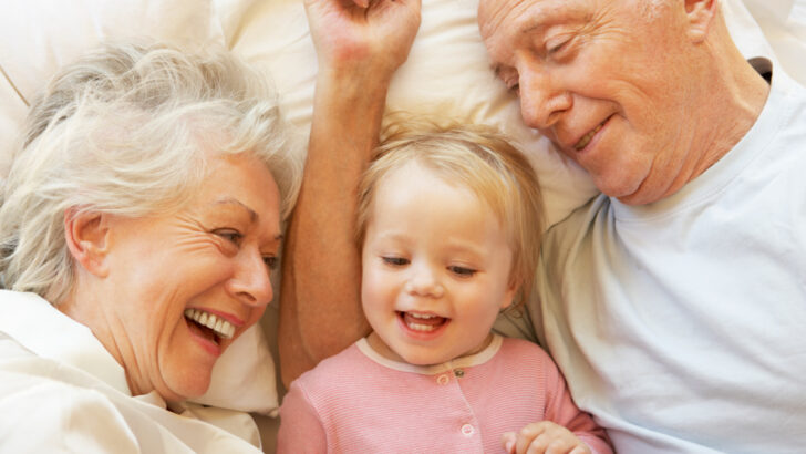grandparents happily babysitting granddaughter, lying in bed together
