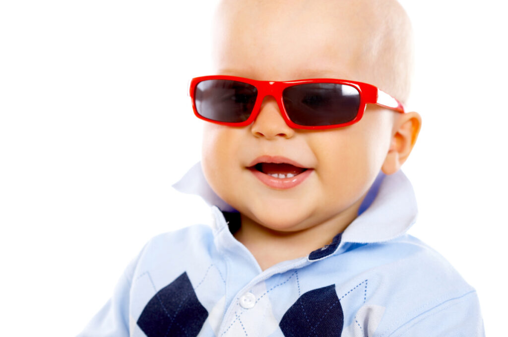 baby boy sitting up with light blue polo shirt and red sunglasses.