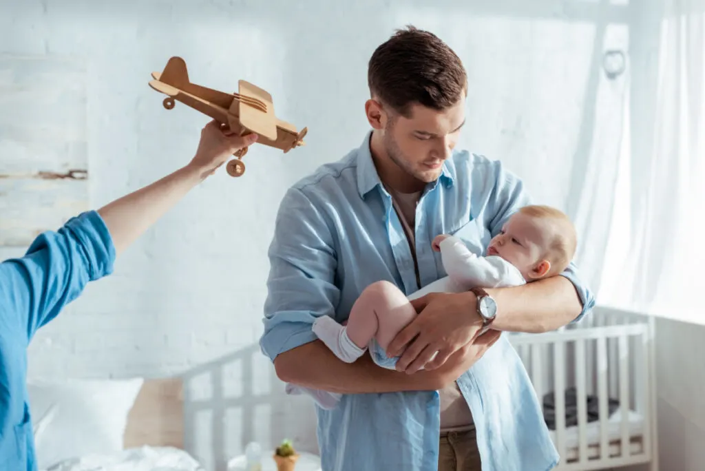 father holding baby boy in nursery with toy airplane in the background