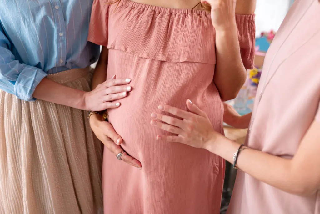 baby shower guests' hands touching pregnant woman's belly