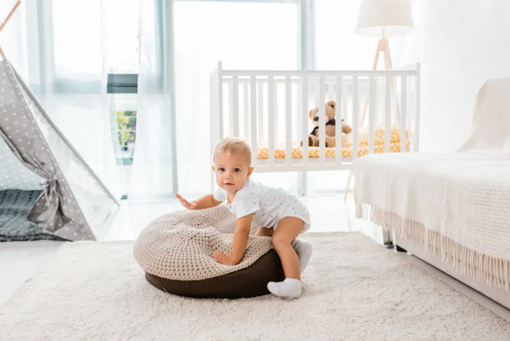 baby playing with cushion, having managed to climb out of his crib