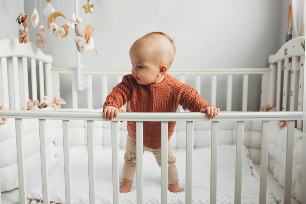 baby standing up in crib with low bars, looking dangerously close to climbing out of the crib