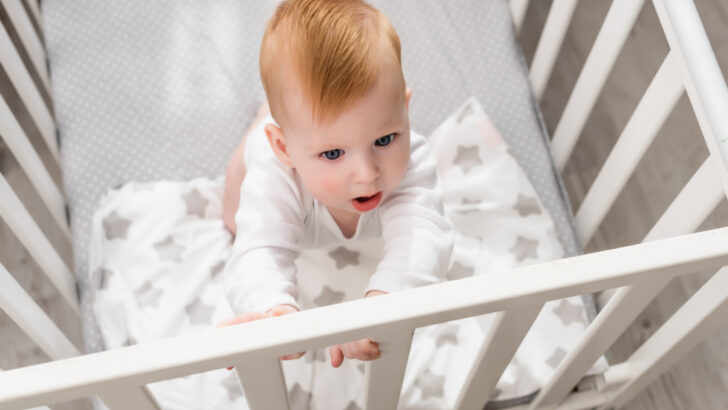 baby in crib, holding crib bars, thinking about climbing out of the crib