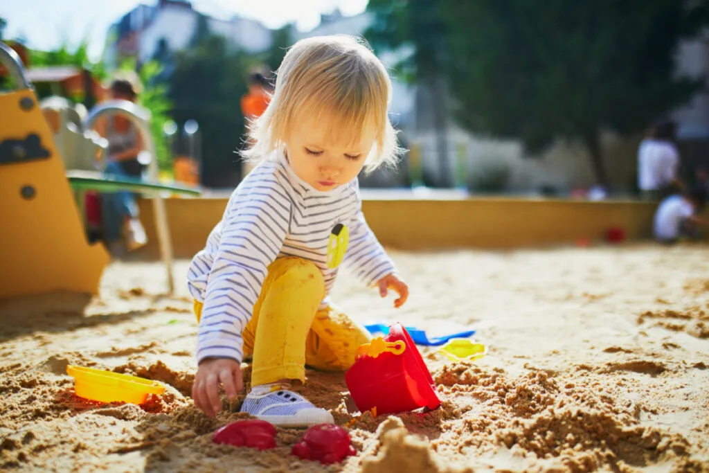 one year old playing outdoors in the sand with sand toys at a local park