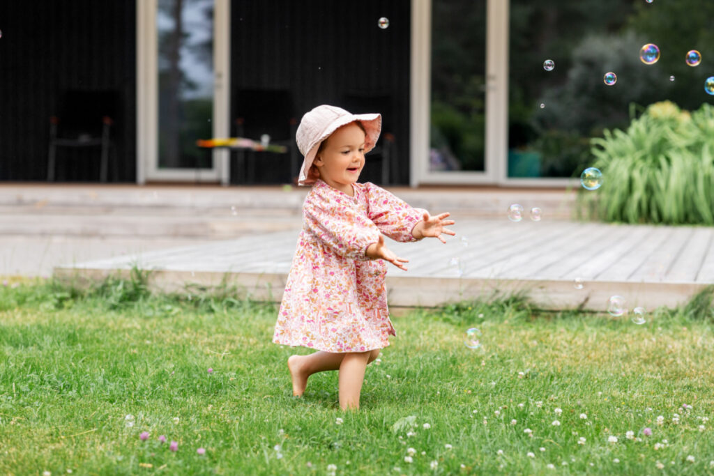 toddler girl in flower dress chasing bubbles outside