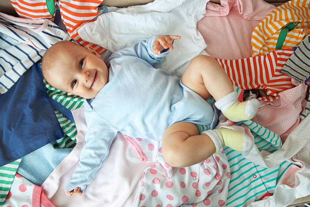 adorable baby lying on top of colorful outgrown baby clothes