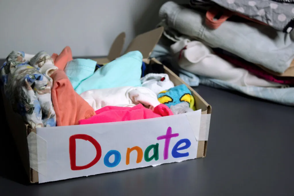 cardboard box full of donations - baby stuff, baby toys and clothes, colorful "Donate" sign taped to side 