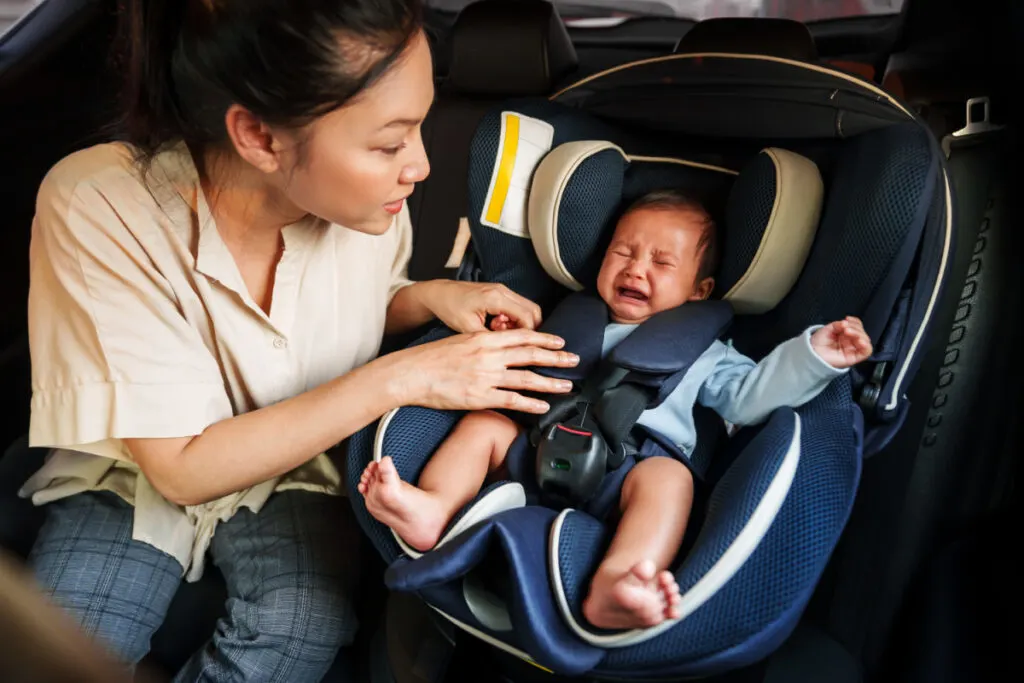 mom trying comfort baby who is crying in their car seat