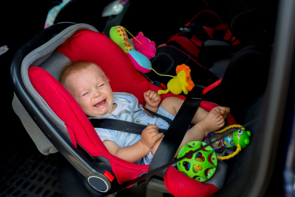 baby crying in rear-facing car seat, with toys at feet.