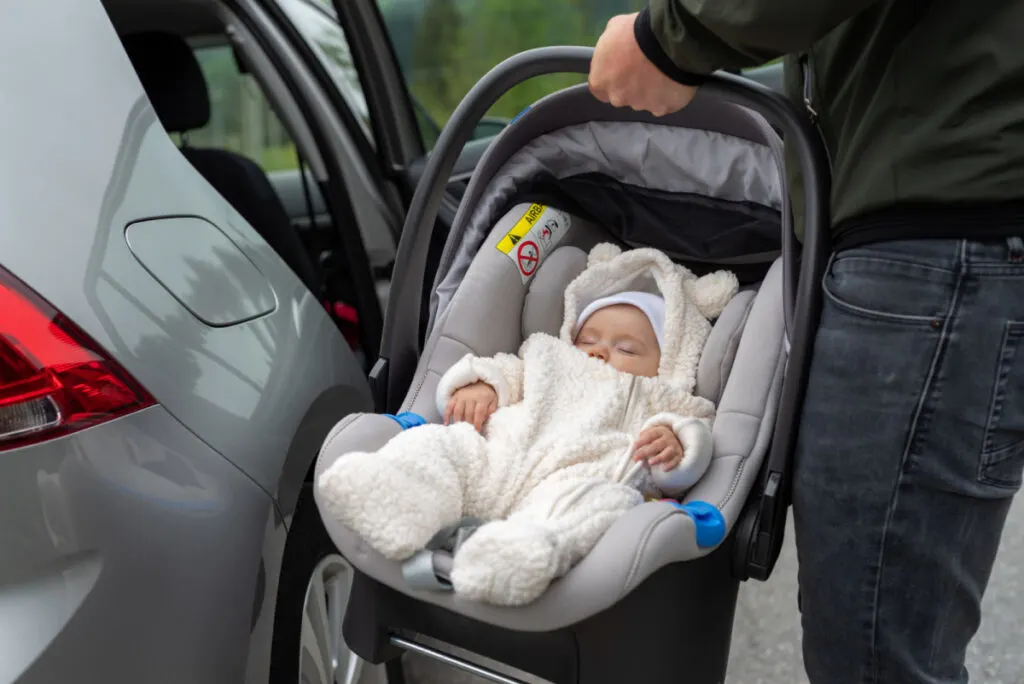 baby stopped crying and is asleep in car seat, dad putting the car seat into the car.