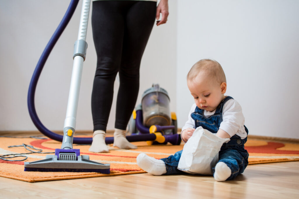 new mom vacuuming with baby sitting on the floor next to the vacuum