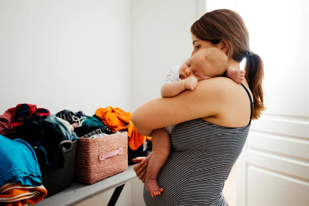 new mom holding baby looking at laundry that needs to get done