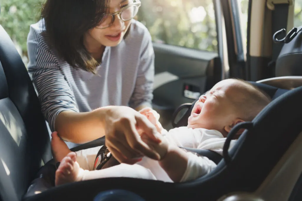 Asian mother trying to stop baby from screaming in car seat.