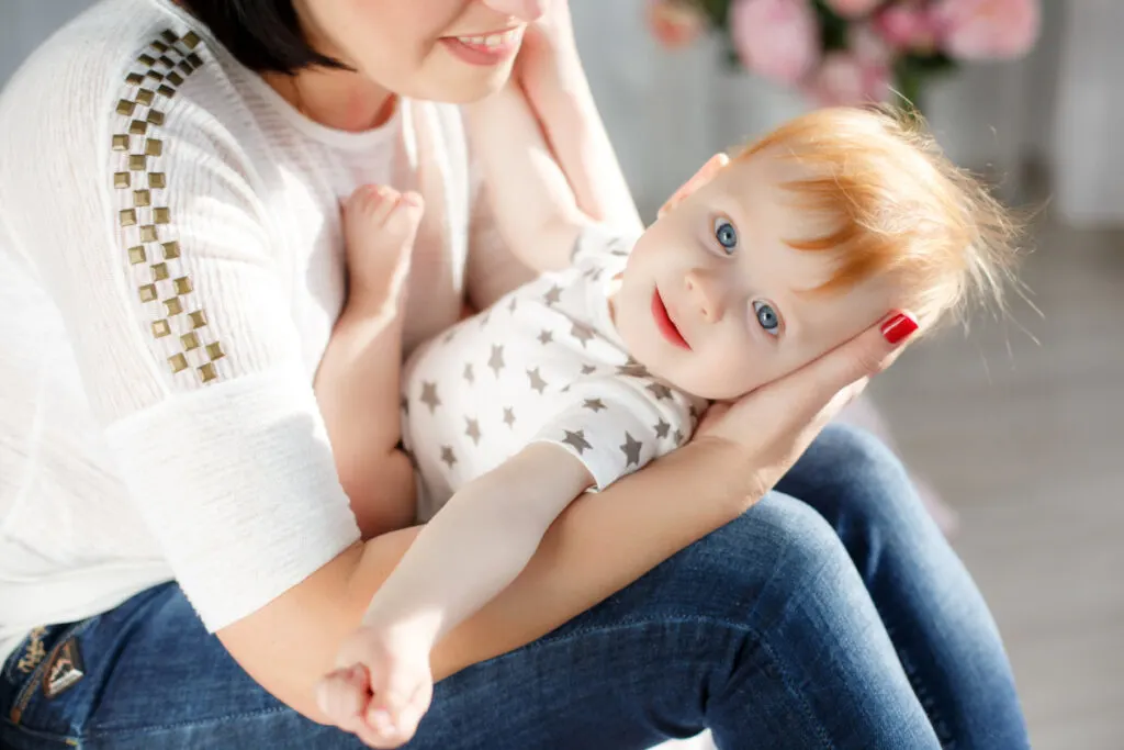 red-headed, blue-eyed baby boy named Maverick, laying on mother's lap and looking at camera.