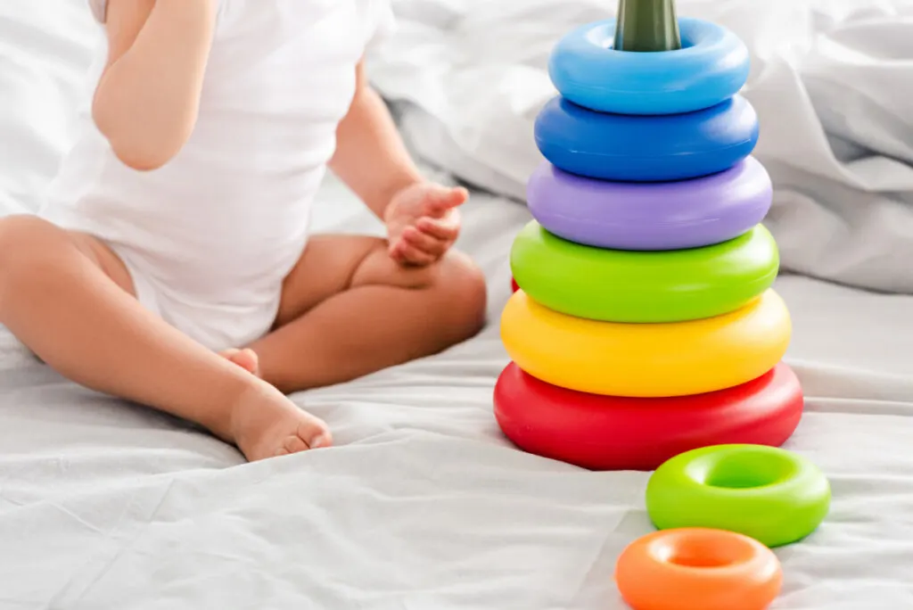 baby sitting up on bed playing with colorful toy rings