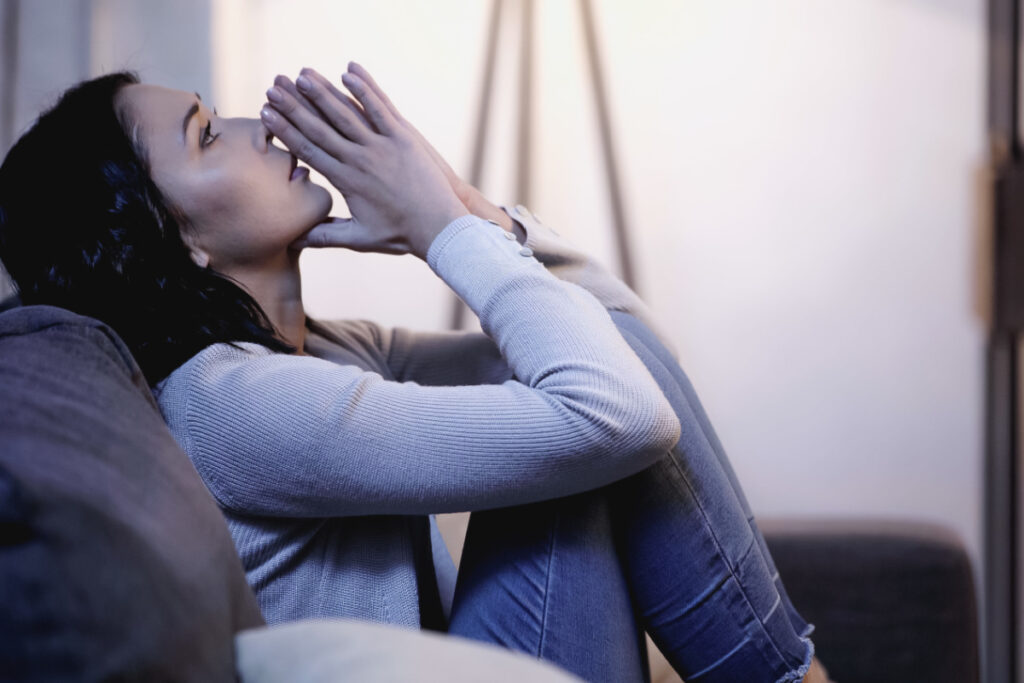 woman struggling with infertility, sitting on couch, praying and looking sad.