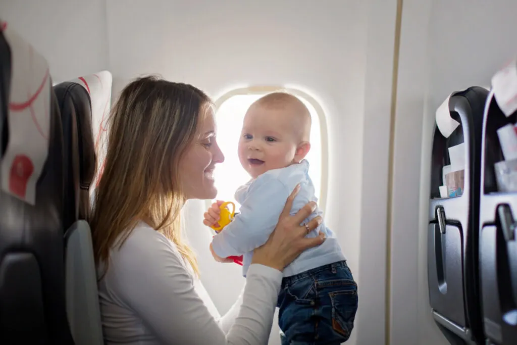 smiling young mom holding and playing with her infant on an airplane.