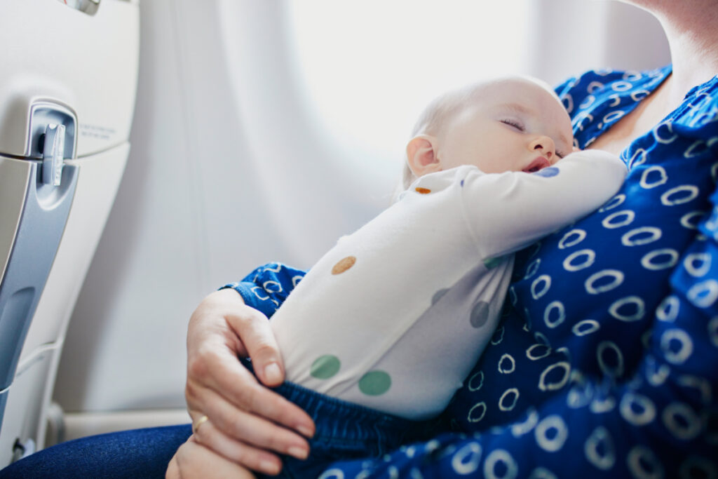 infant sleeping on mother's chest while traveling on a plane.