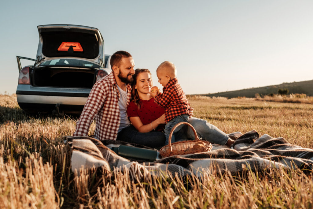 a young family taking a picnic break from their long car journey with a baby