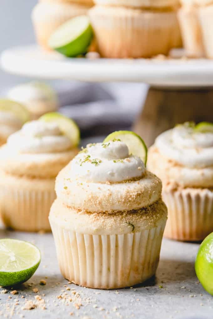 key lime cupcakes with key lime frosting, graham cracker crumbs and lime zest with a lime wedge, next to halved limes.