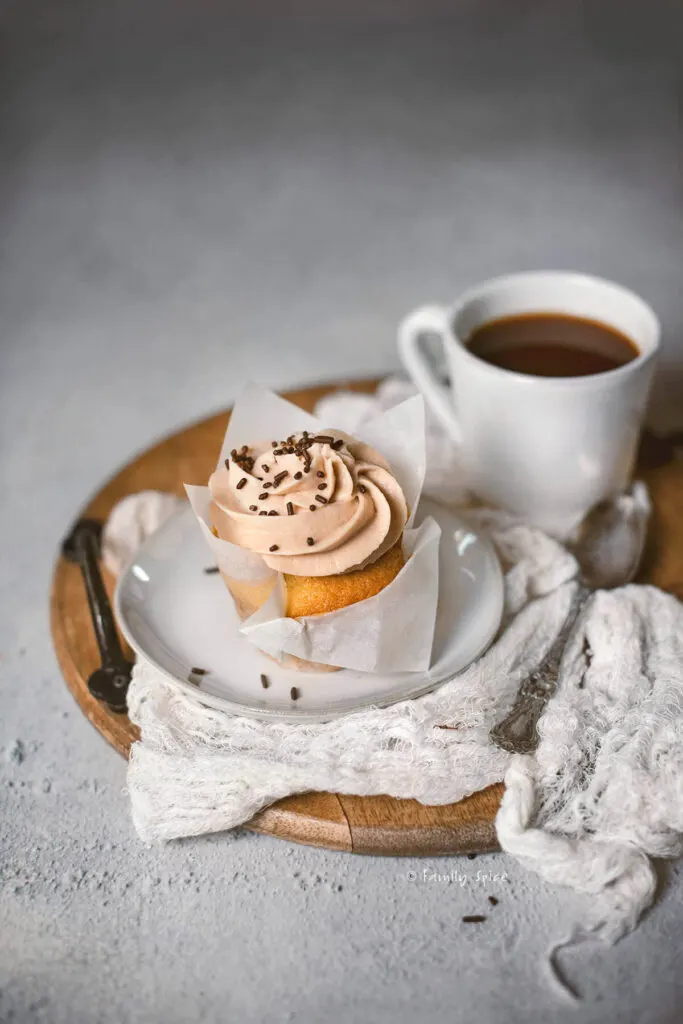 Bailey's cupcake with chocolate sprinkles on wooden tray with coffee cup and spoon.