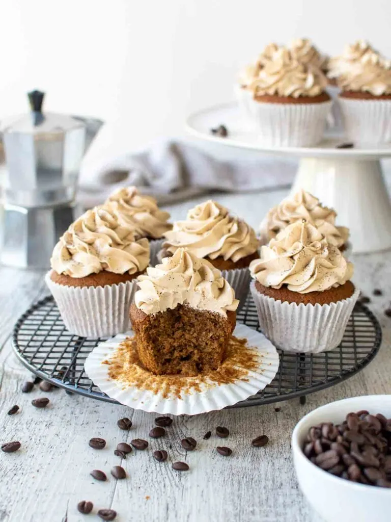 coffee cupcakes with coffee buttercream frosting, sprinkled with espresso powder, coffee beans in background and sprinkled all around.