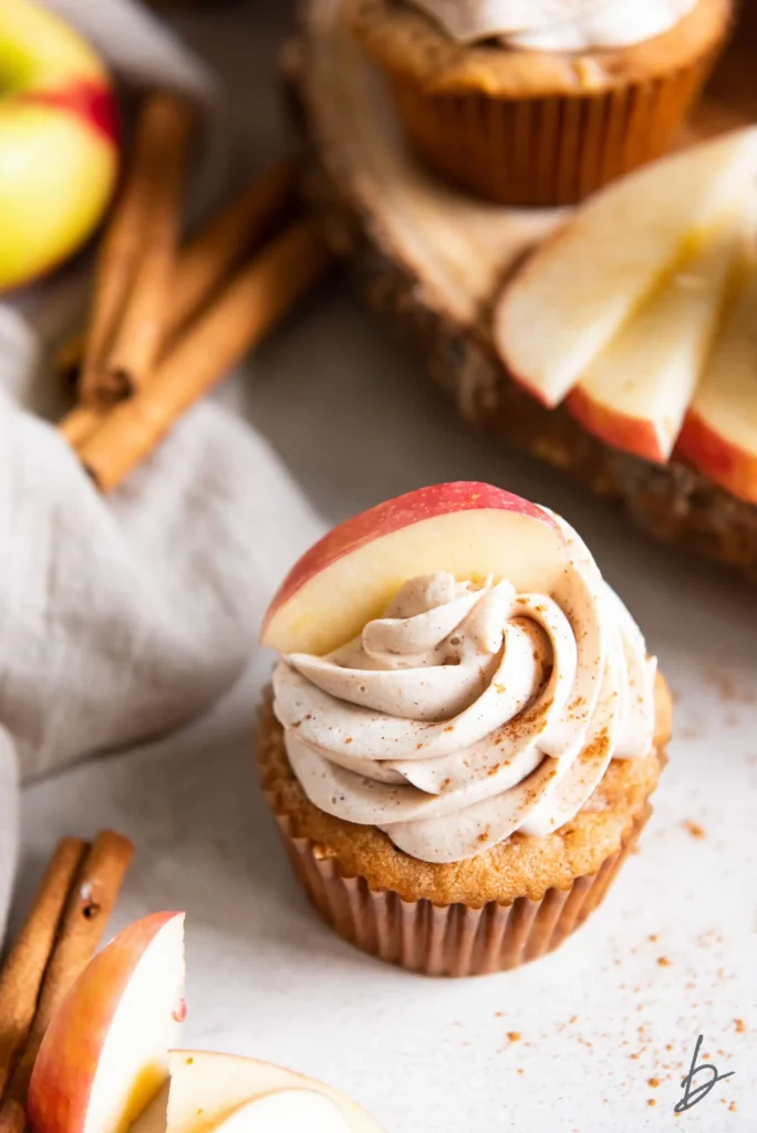 apple spice cupcake with cinnamon sticks and apple slices in background.
