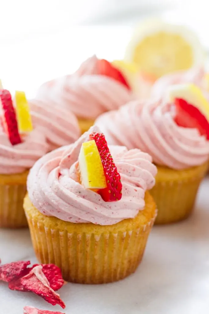 strawberry lemonade cupcakes with strawberry frosting and a strawberry and lemon slice on top.