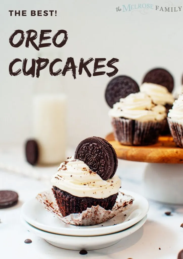 oreo cupcake with white cream cheese frosting and oreo cookie on top, cake stand with more cupcakes in background.