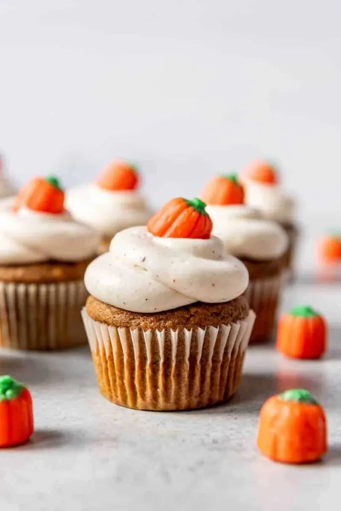 pumpkin cupcakes with spiced cream cheese frosting and pumpkin candy corns on top.