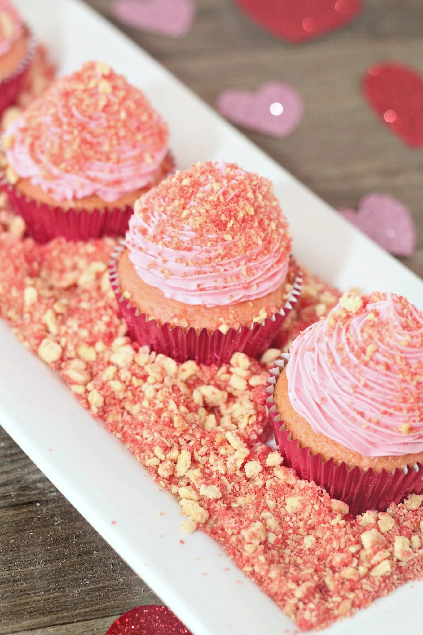 strawberry crunch cupcakes with pink wrappers and pink frosting on white ceramic tray.