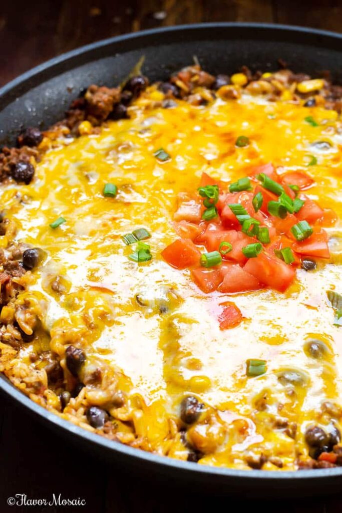 Mexican beef and rice casserole with cheese, tomatoes and scallions on top.