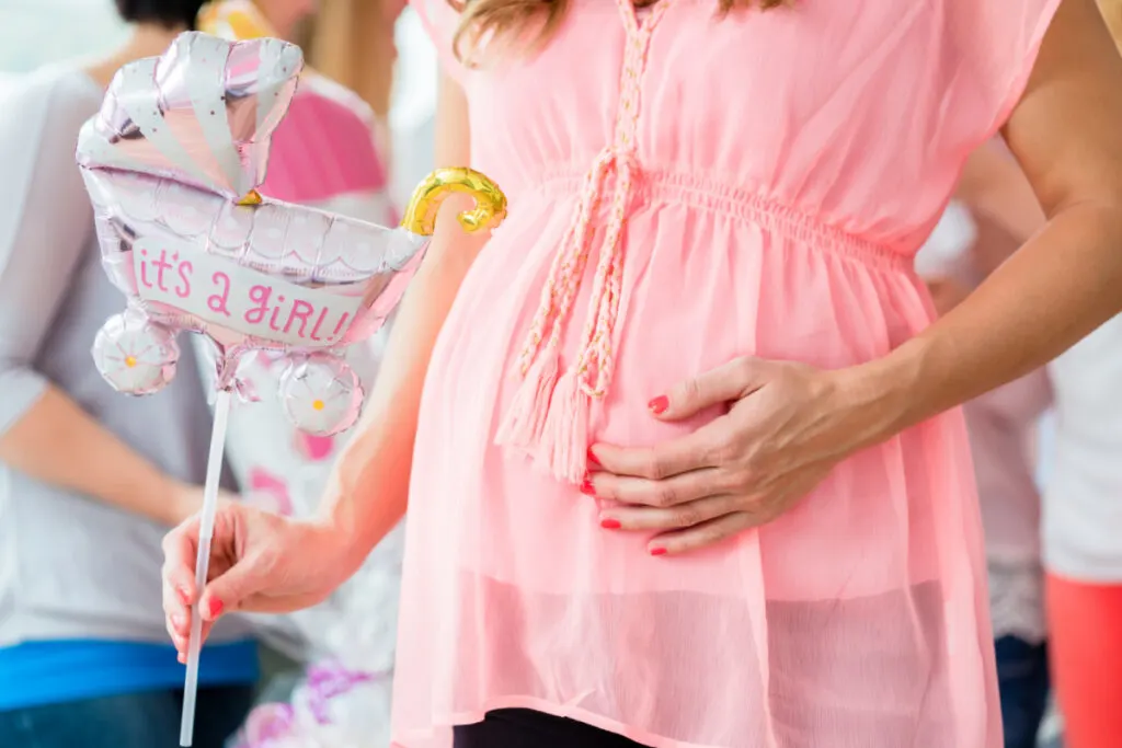 Pregnant woman showing her baby belly and "It's a girl" balloon, celebrating baby shower party with friends