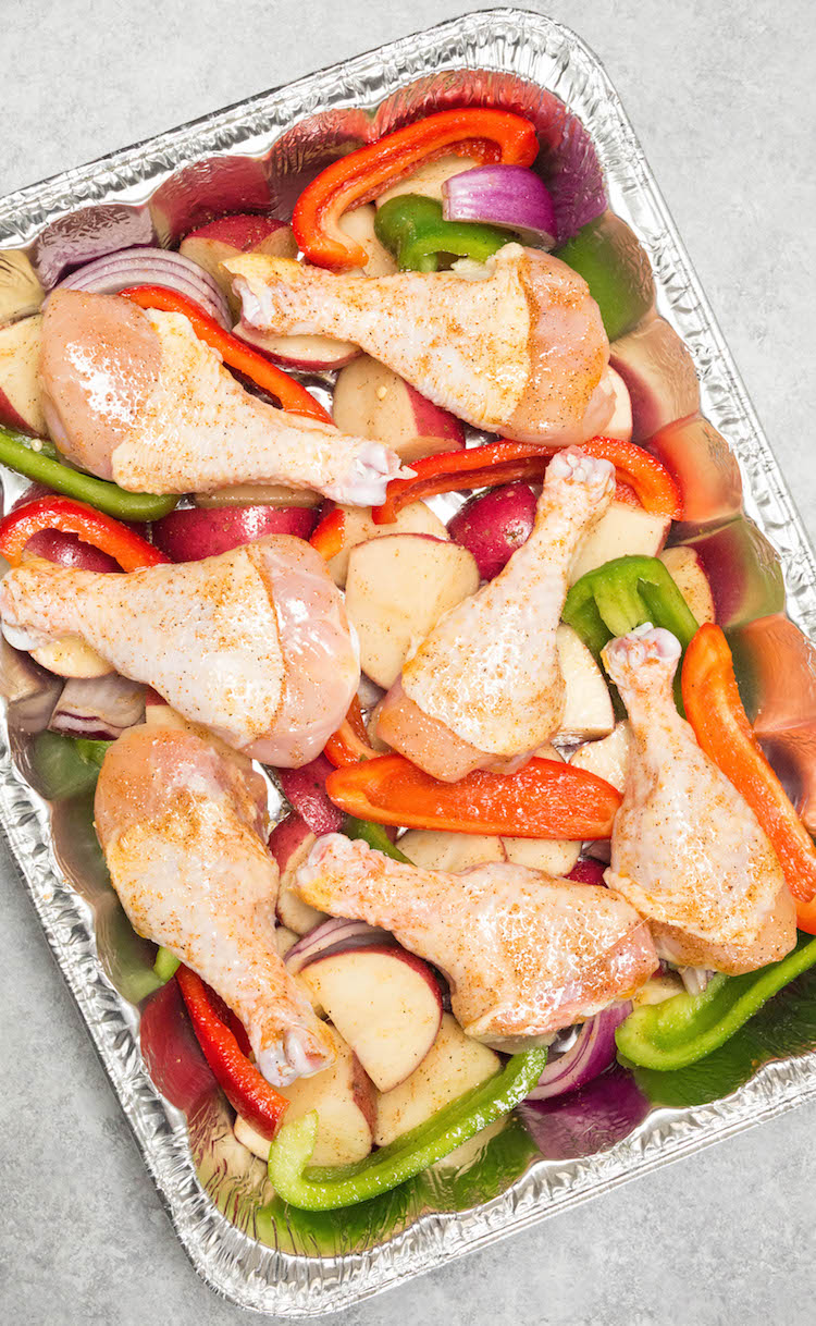 chicken legs and veggies with seasoning in foil casserole dish for freezing.