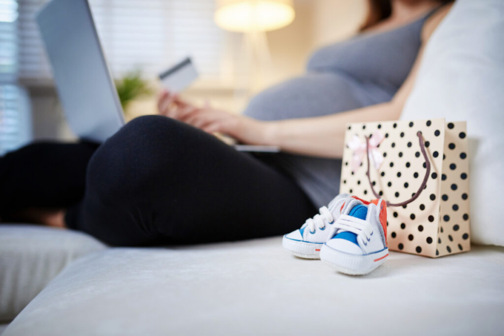 woman creating baby registry, sitting with computer on lap and credit card in hand, baby shoes close up.