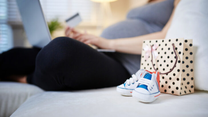 woman creating baby registry, sitting with computer on lap and credit card in hand, baby shoes close up.