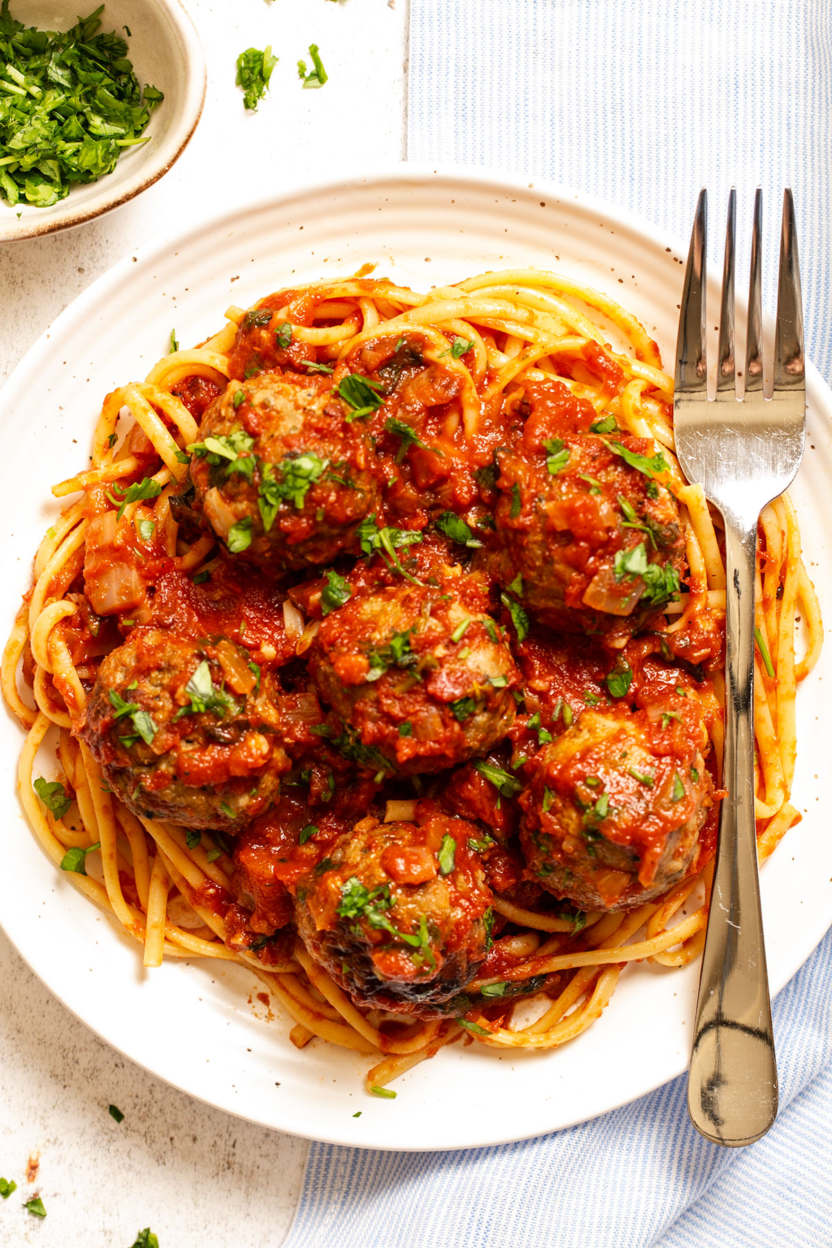 Italian meatballs in sauce on top of pasta with fresh parsley, on plate with fork.