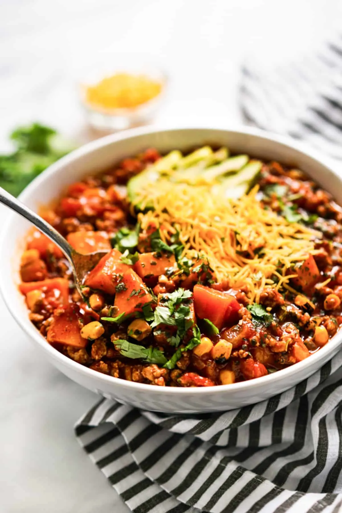 turkey sweet potato chili in a bowl with shredded cheese and avocados