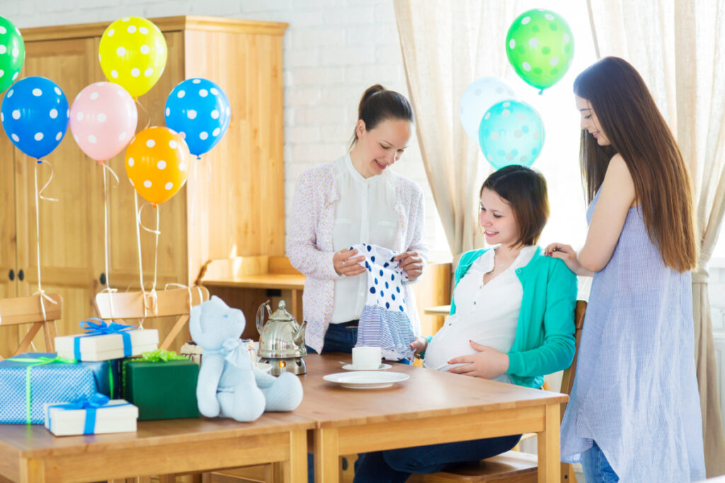 pregnant woman at baby shower with friends, showing her an article of baby clothes.