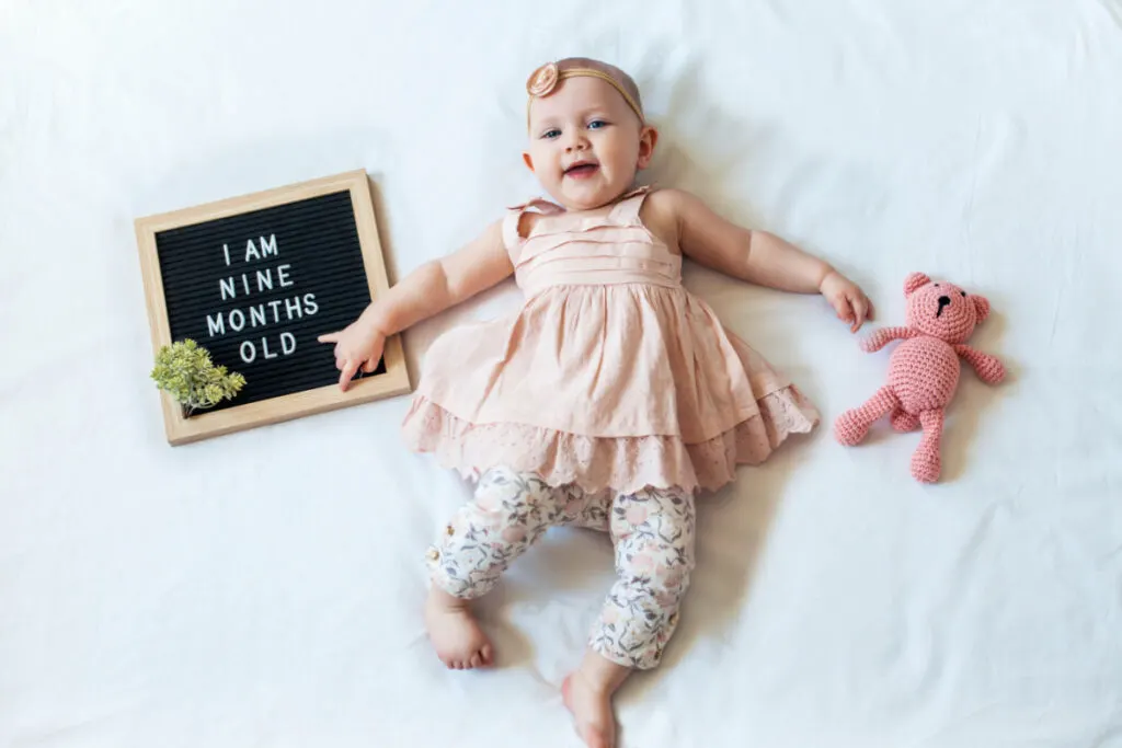 9 month old baby girl lying on blanket with sign that says "I am nine months old"